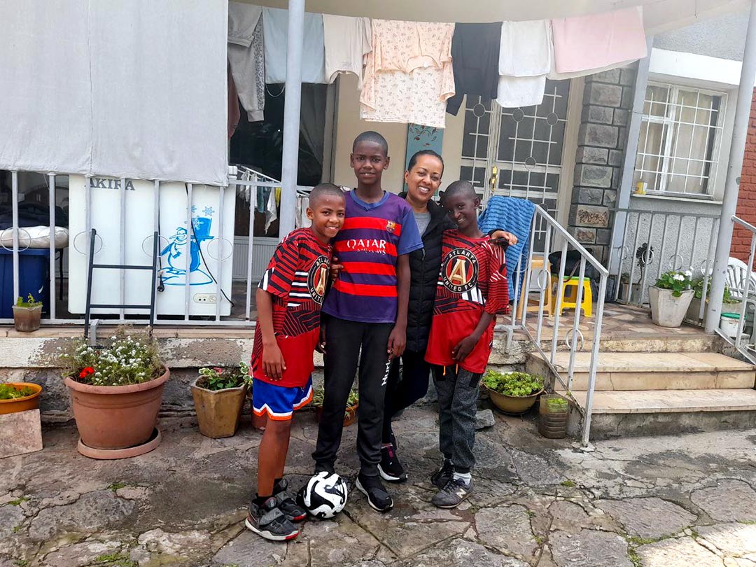 three boy post with their foster mom in front of their house in Ethiopia