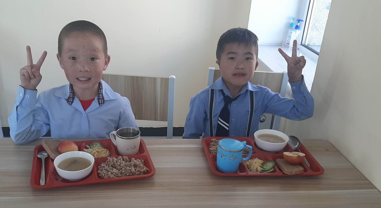 Two little boys hold up peace hands with lunch tray