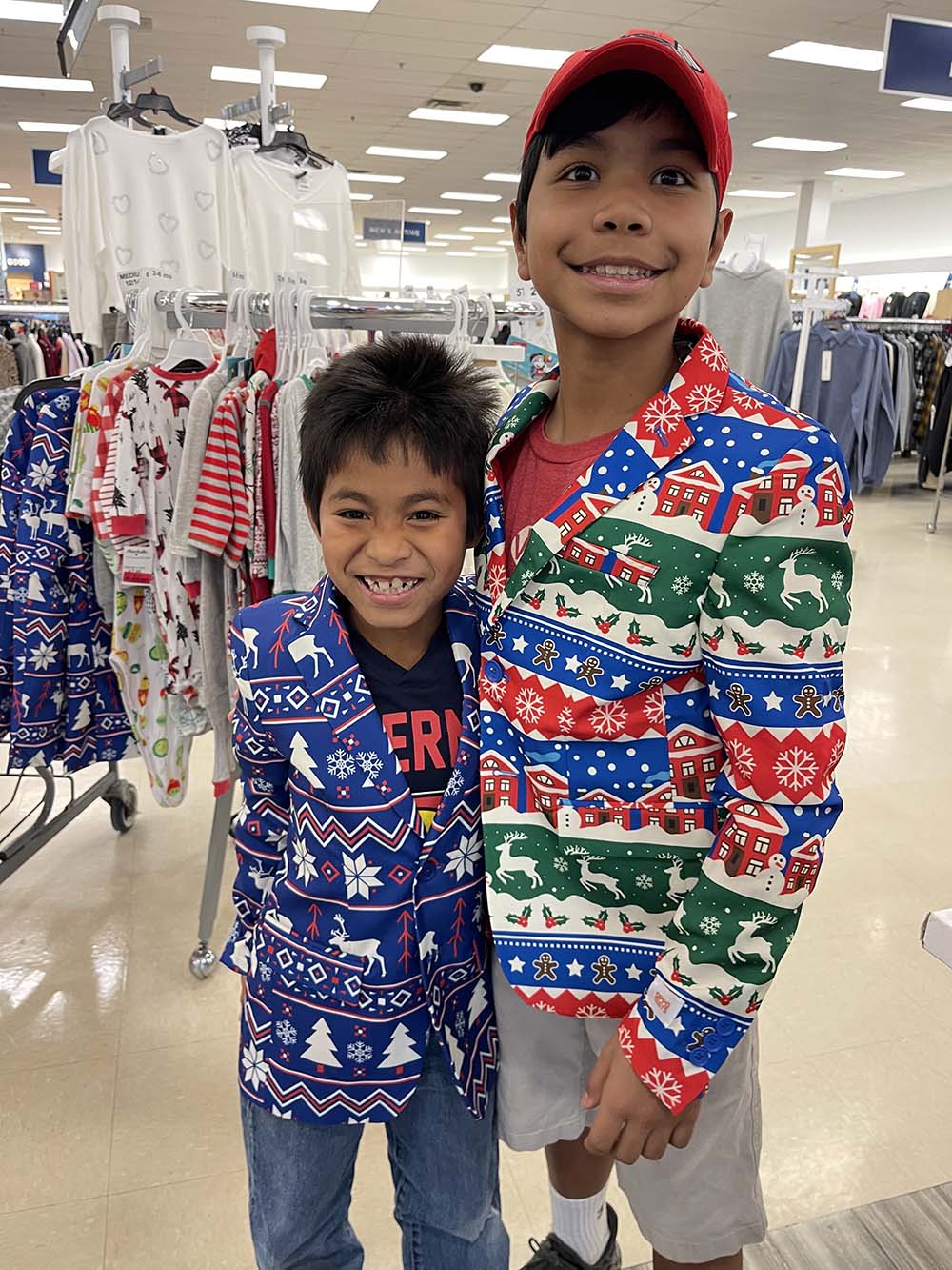Two boys in department store smile in silly Christmas blazers