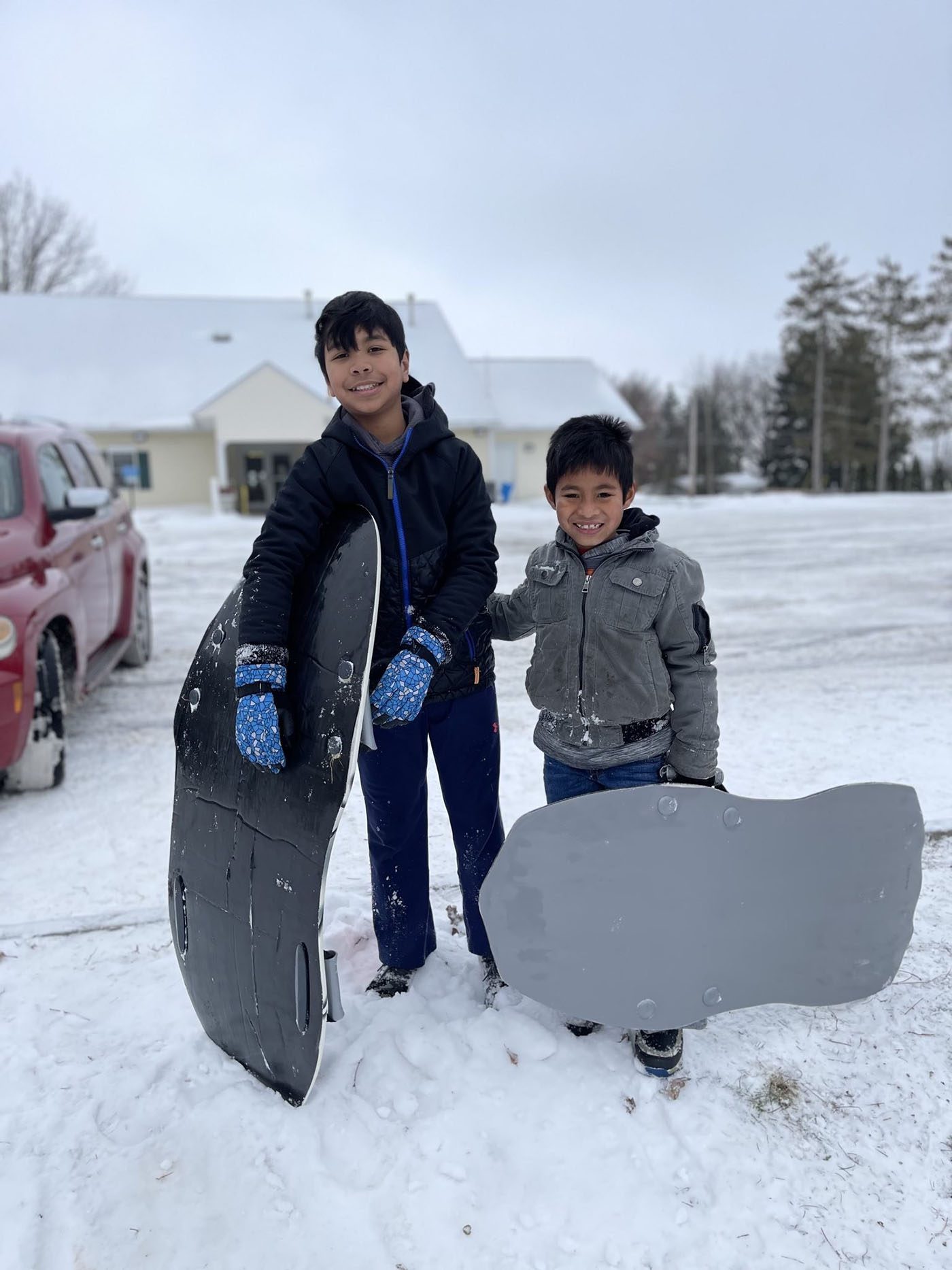 Two boys hold sleds in snowy winter