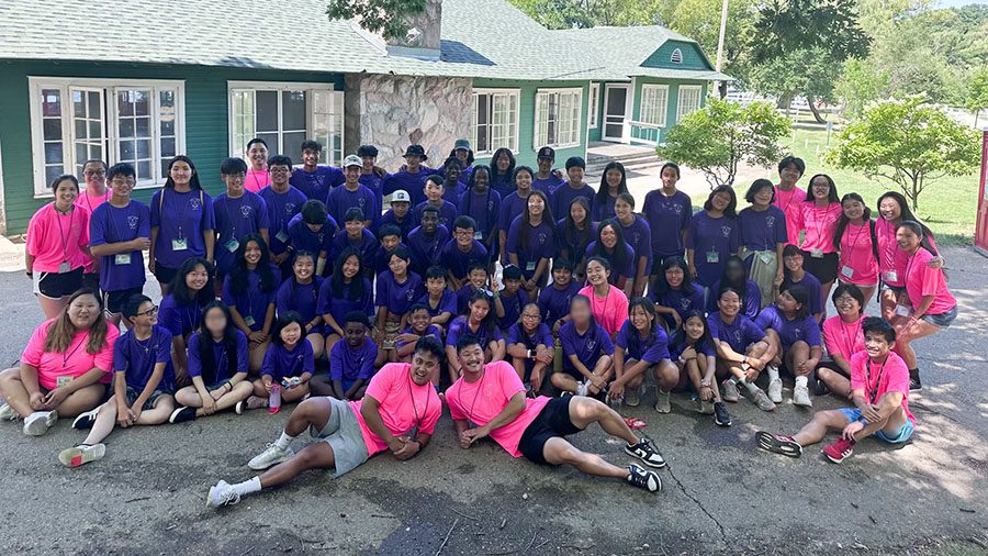 Group of campers and counselors in purple and pink t-shirts gather for a group photo