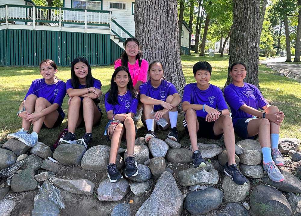 Group of kids in purple shirts sits on rocks smiling