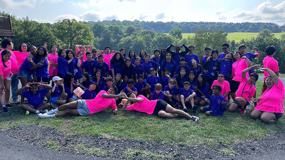 Group of campers and counselors in purple and pink t-shirts take a silly photo