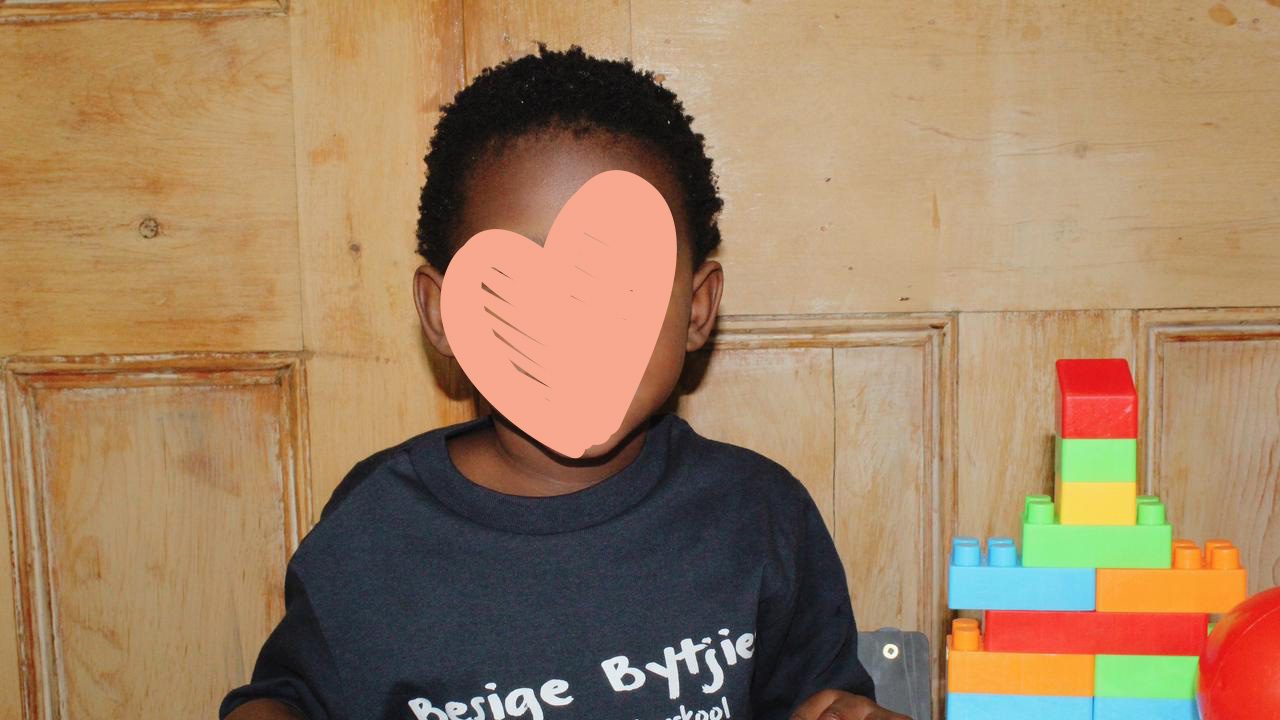 Little girl in oversize t-shirt smiles next to a stack of blocks