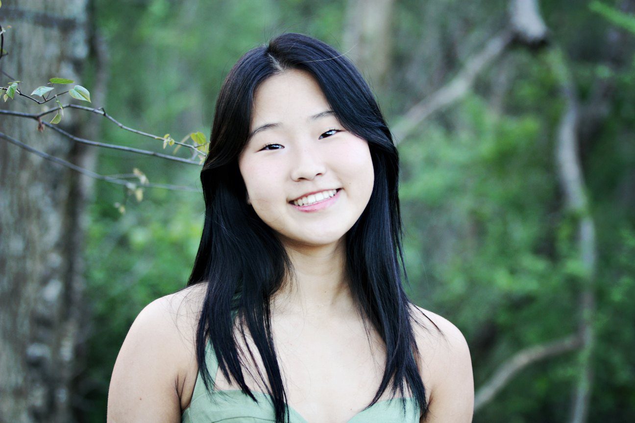 Girl in green dress smiles in front of a tree