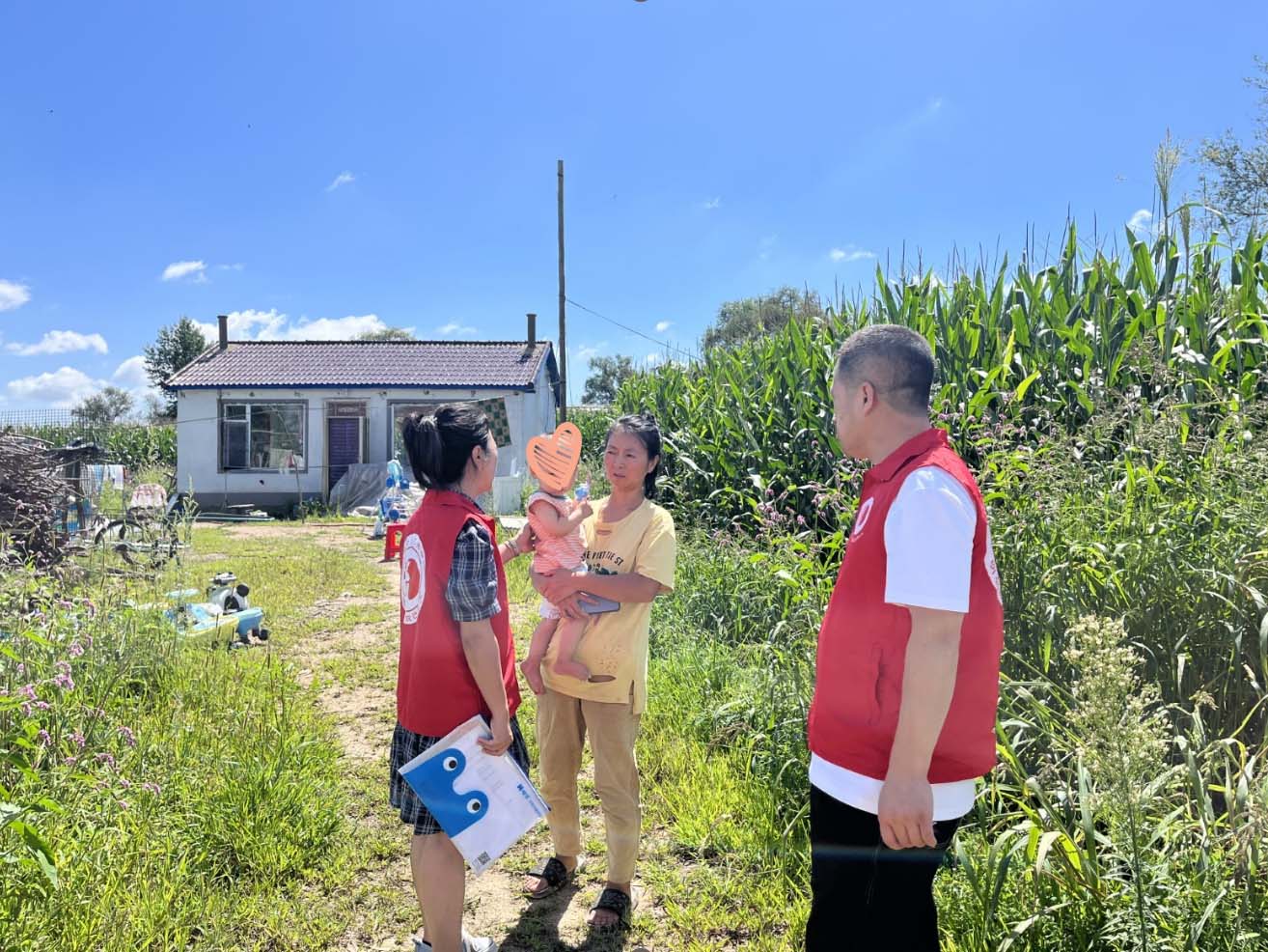 Group of people gather to talk outside in a field, a mother holds a baby