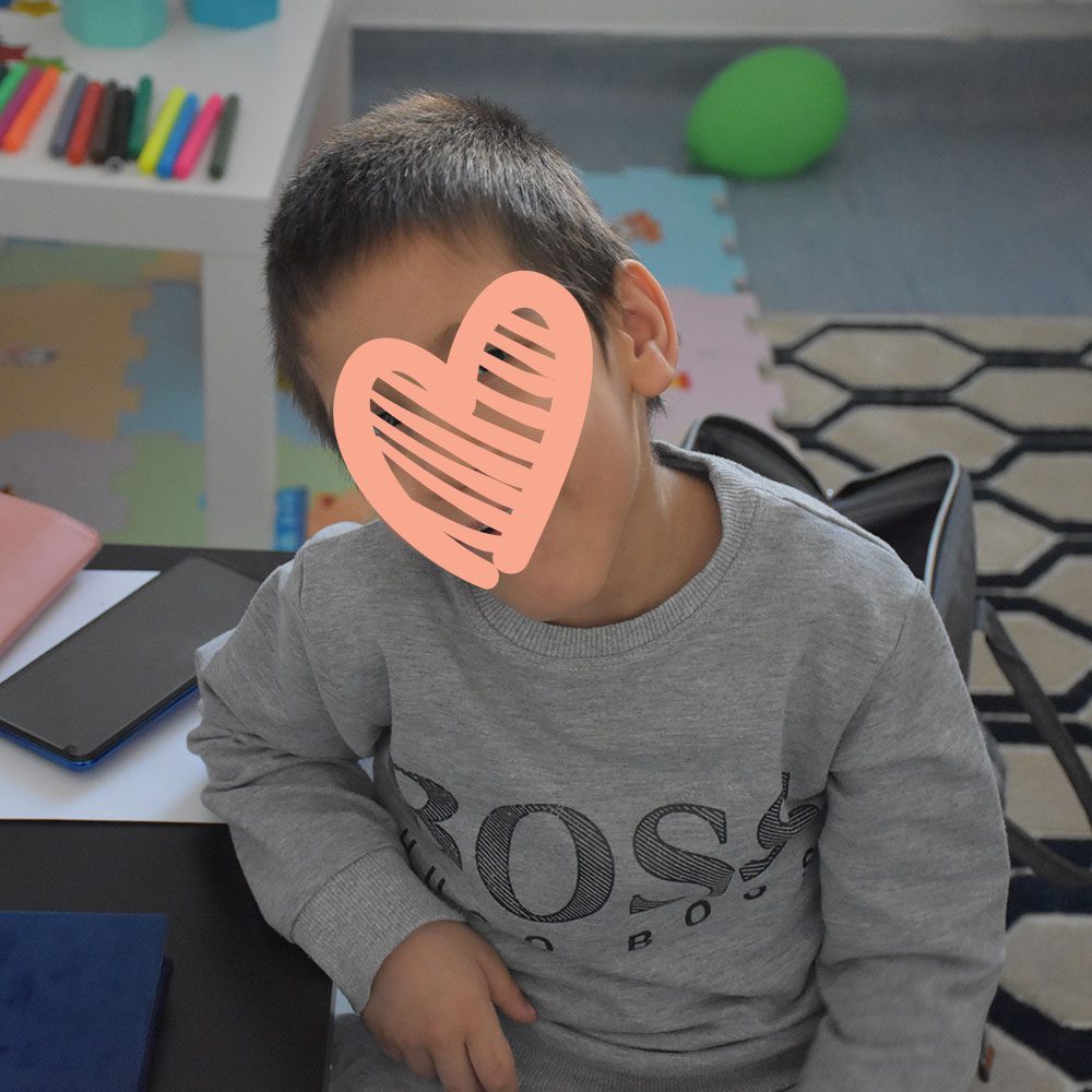 Little boy in grey sweater smiles at camera while sitting at desk