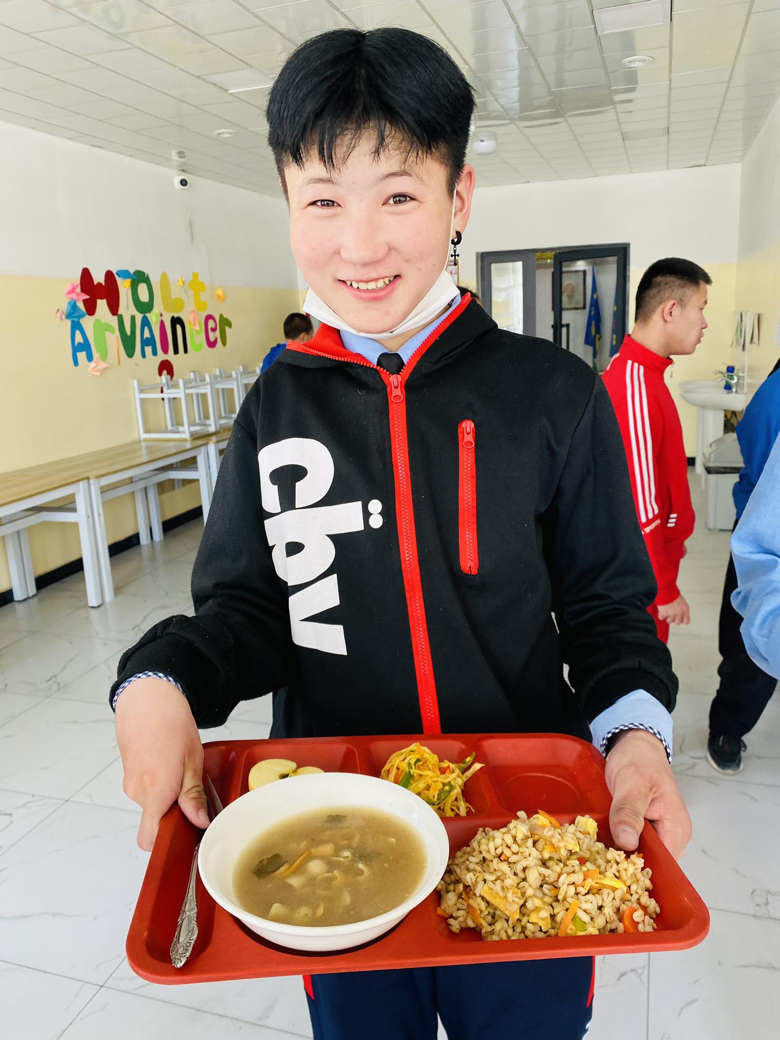 Young person holds school lunch tray, smiling.