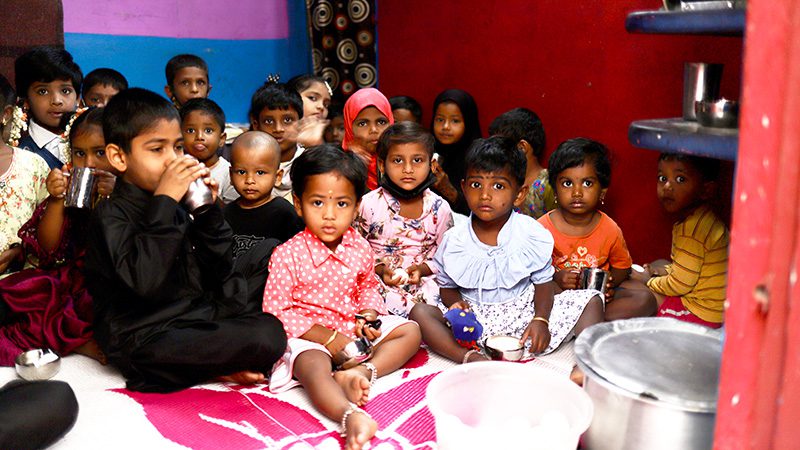 Children gather in a doorway to eat breakfast in India