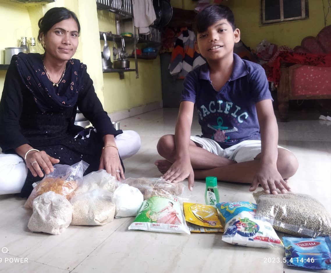 Mother and son sit cross-legged on floor with food donations in front of them