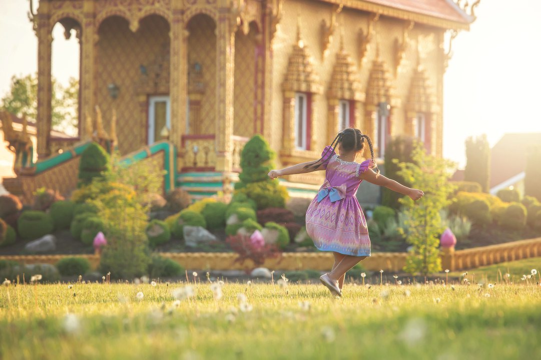 A little girl in a dress runs in front of a Thai temple