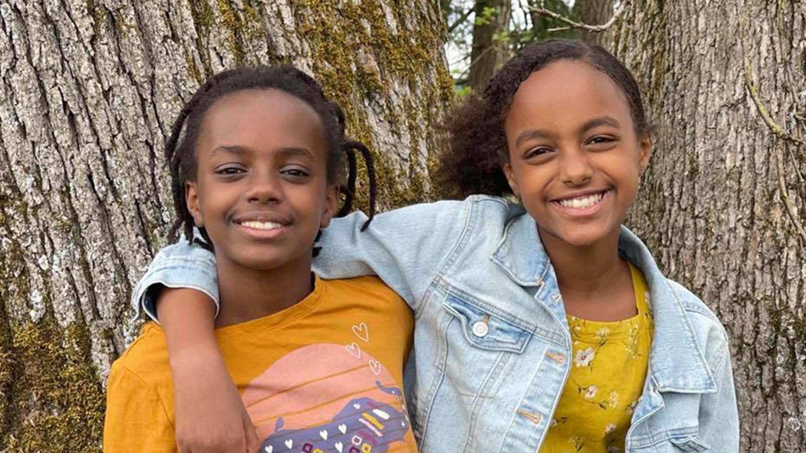 Ethiopian adoptee sisters hug and smile in front of trees