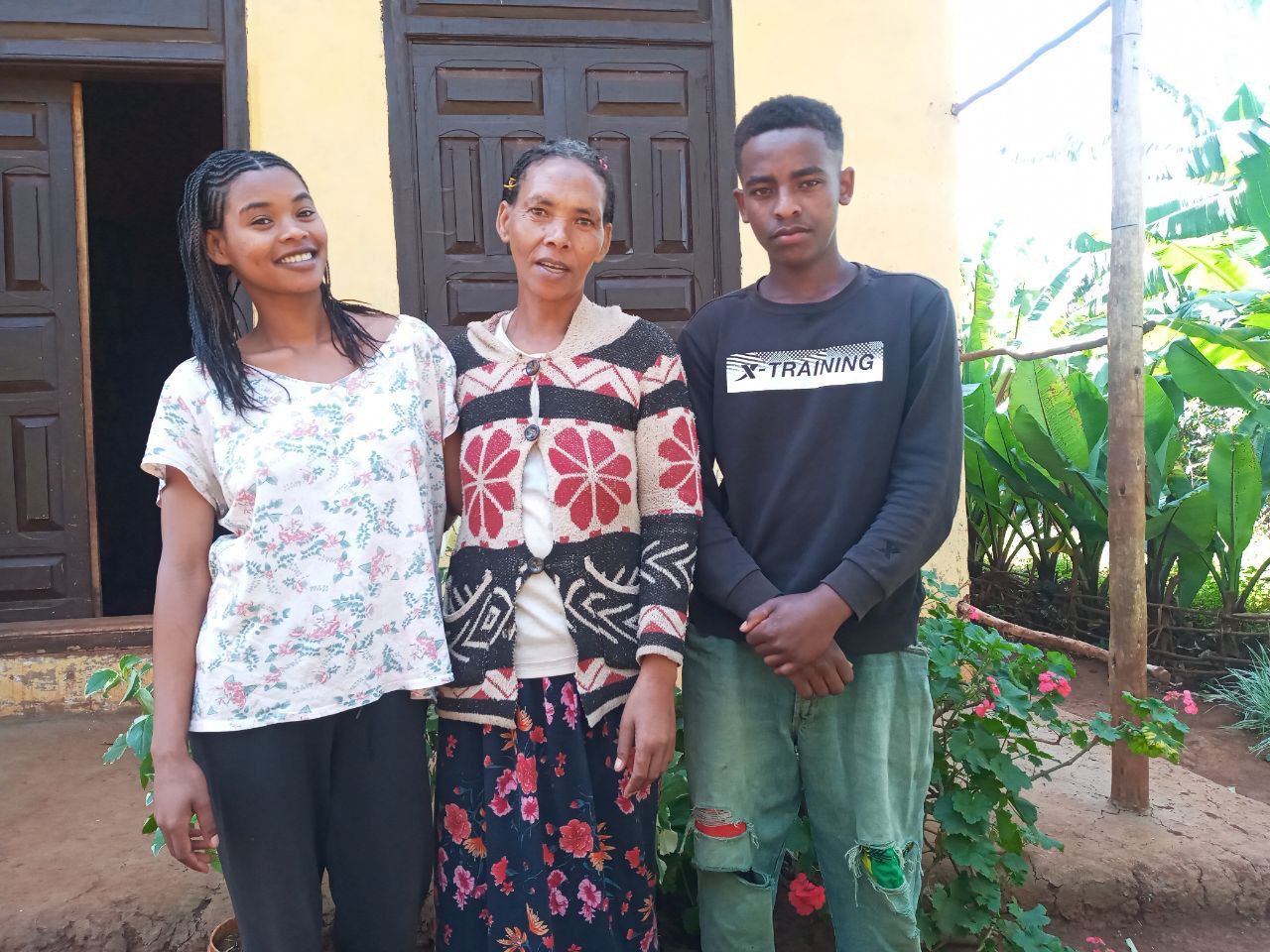 Woman stands in front of house with her son and daughter