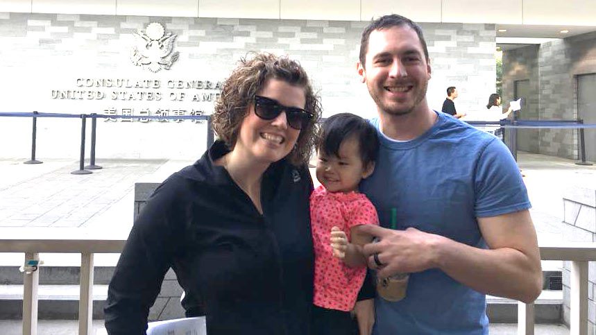 mother and father in China Consulate holding their toddler daughter they adopted through Holt