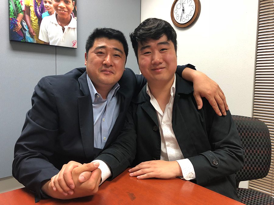 Father and son hold hands and smile at camera