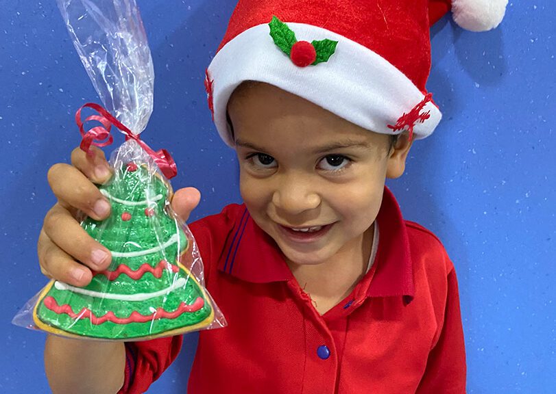 A toddler in a Santa hat holds a Christmas cookie