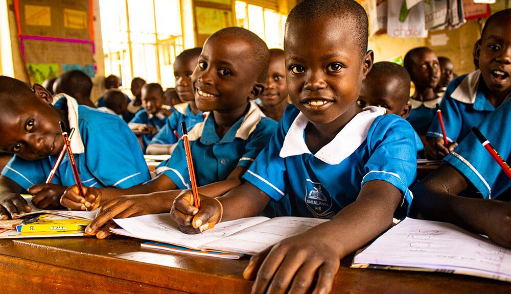 Little girl in school uniform smiles at camera in classroom with book in front of her