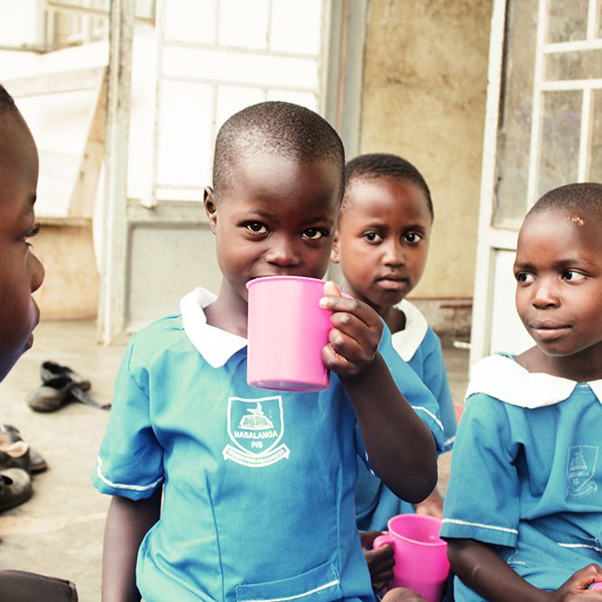 Little girl in school uniform drinks water with her friends