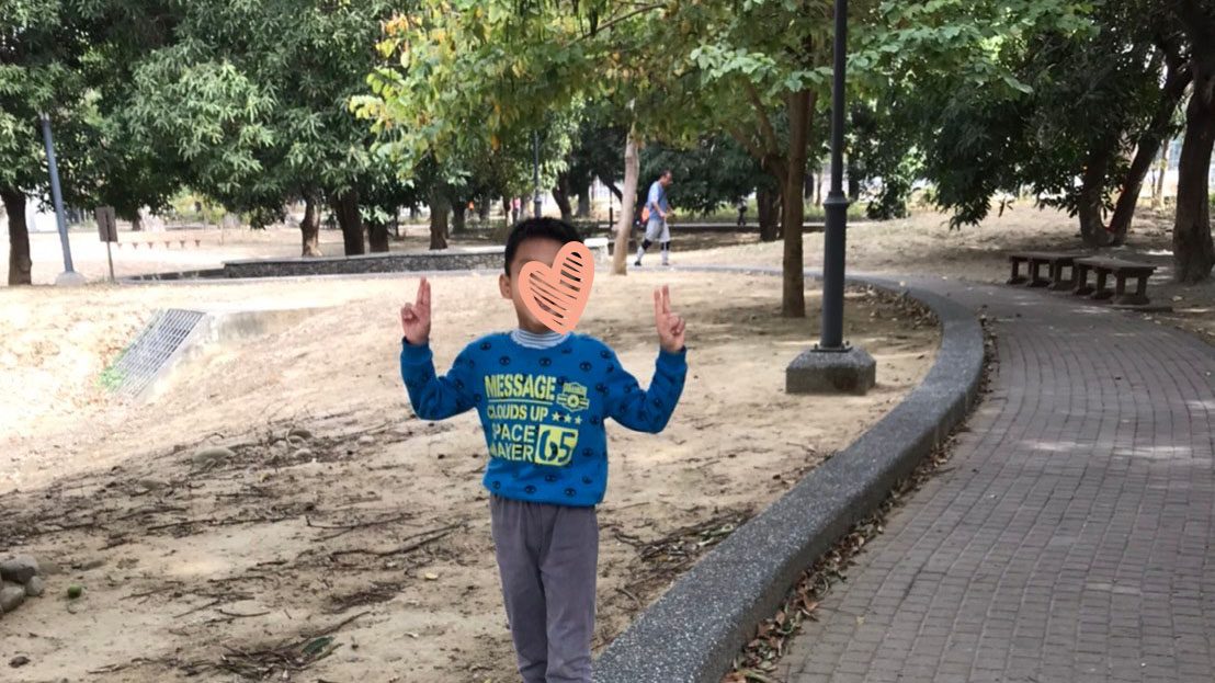 Little boy holds up peace sign and walks along sidewalk border