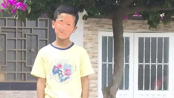 Boy in yellow shirt smiles in front of house