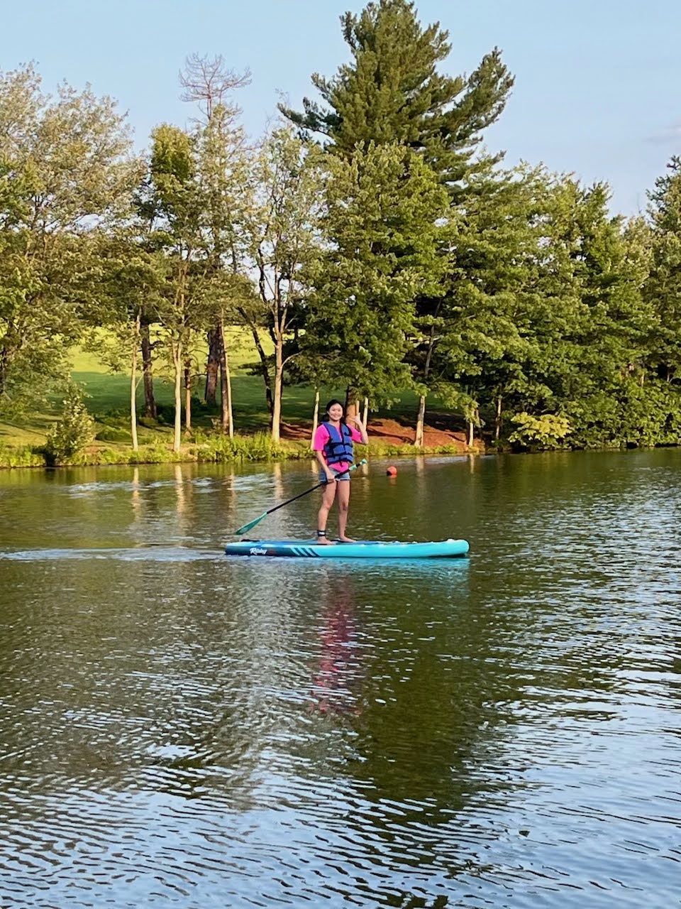 Girl stands on stand up paddleboard on lake