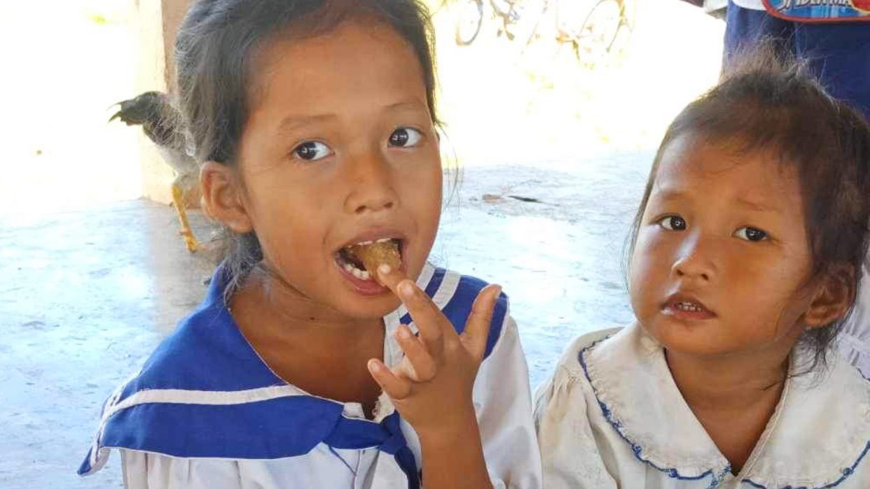 Two little girls smile at camera eating