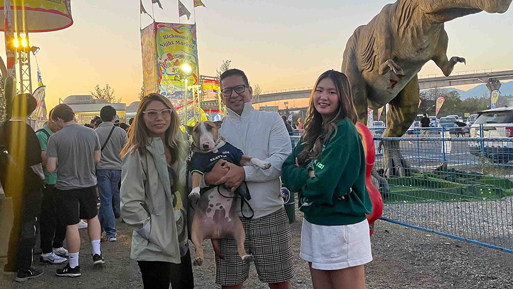 Family with dog stands outside at a night market and smiles at camera