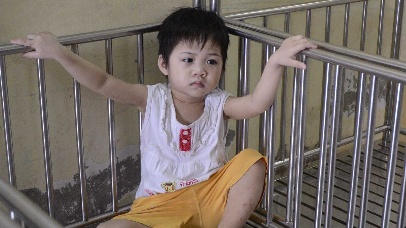 A child sits in a bare crib in an orphanage in Vietnam.
