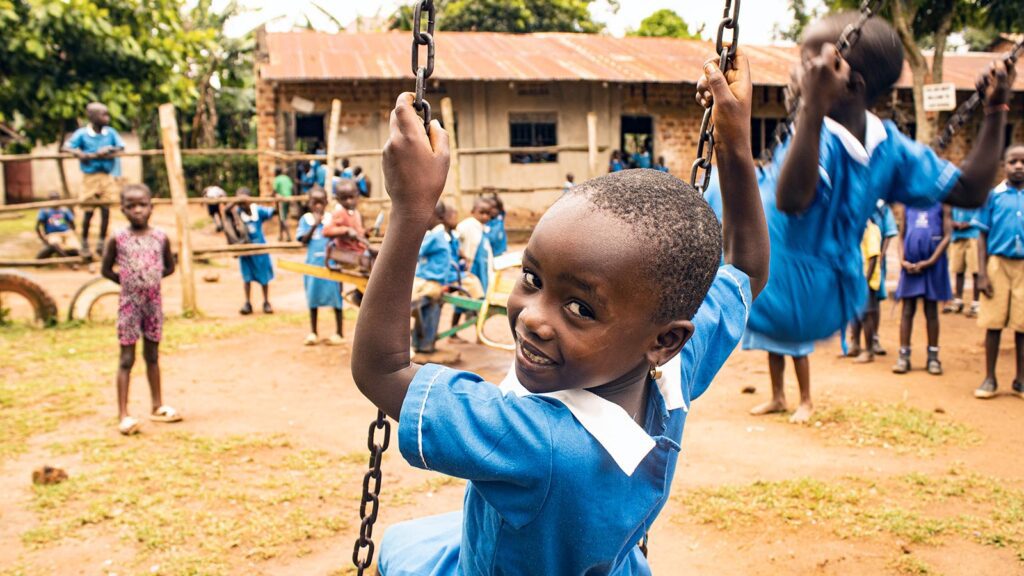 Little girl in a blue school uniform swinging on a swing and looking behind her at the camera