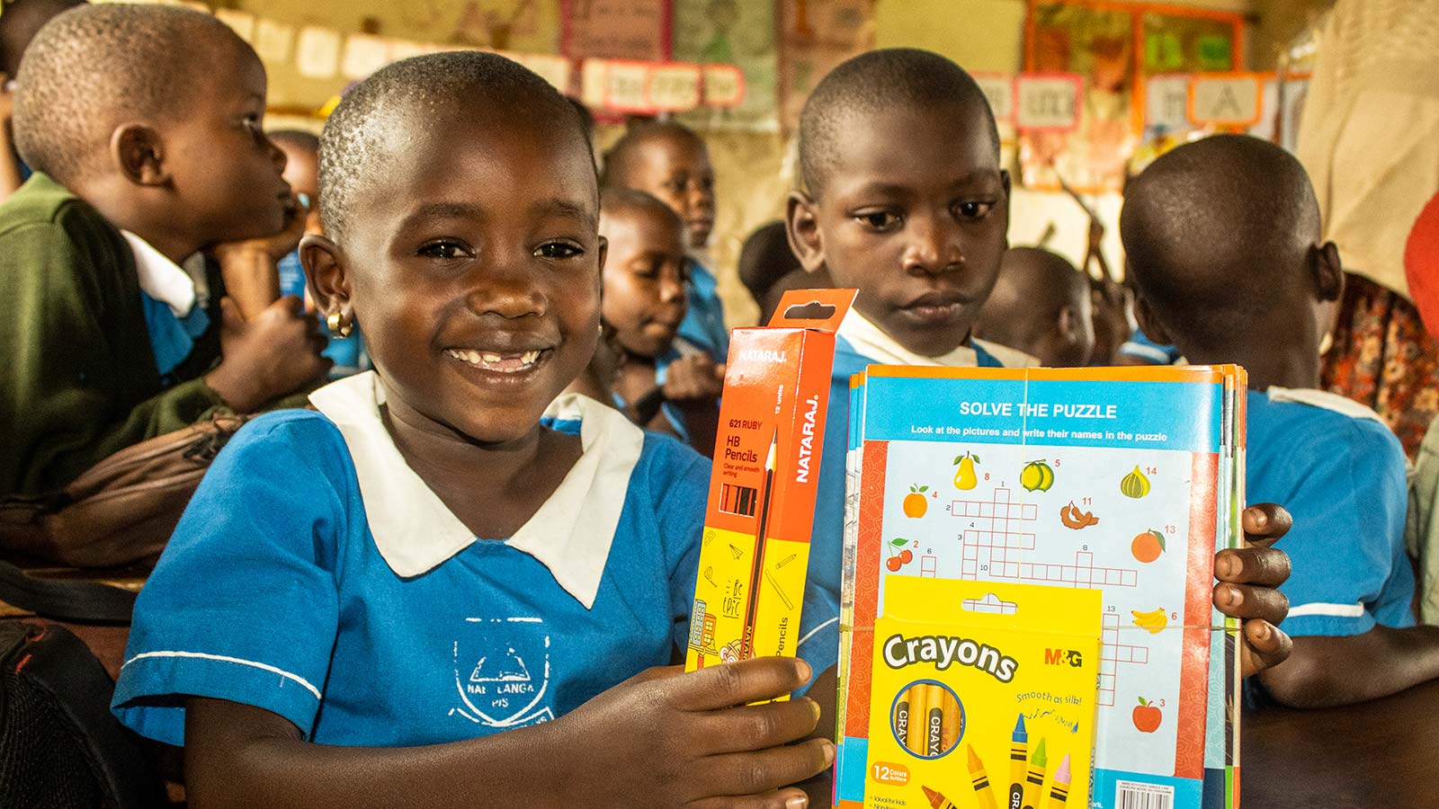 Young girl in a blue school uniform holds up new holt donated school supplies and smiles for the camera.