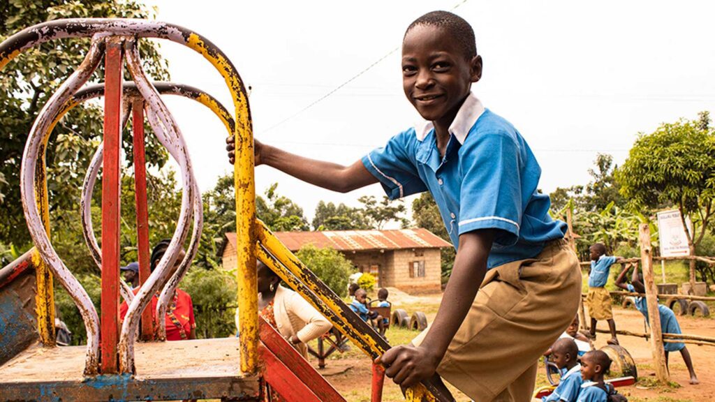 Young boy in a blue school uniform climbs up the ladder of a slide on a playground at school.