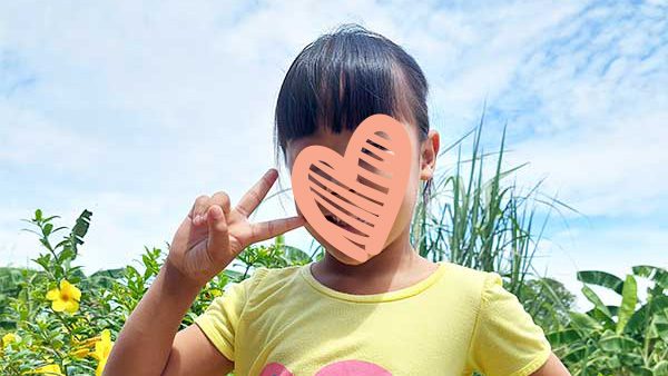 Little girl in a yellow shirt holds up a peace sign