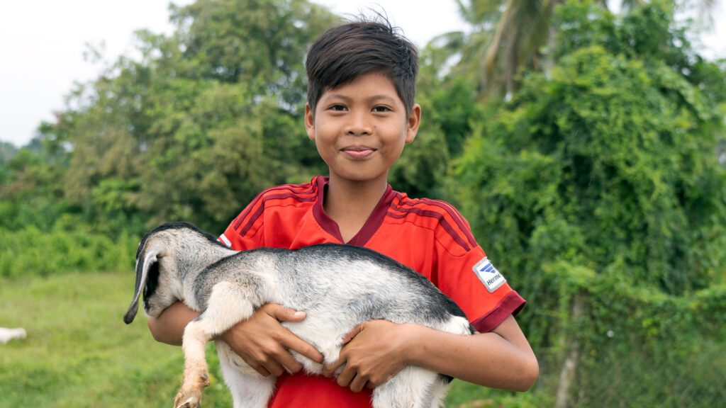Little boy holding a goat in a field