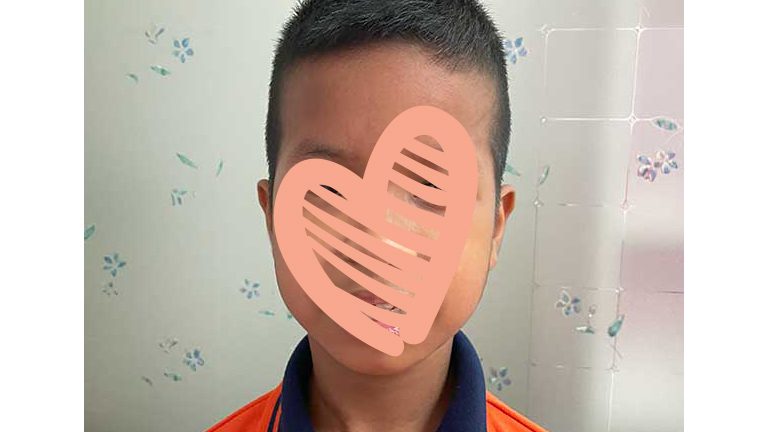 Little boy in orange shirt with black collar smiels at camera