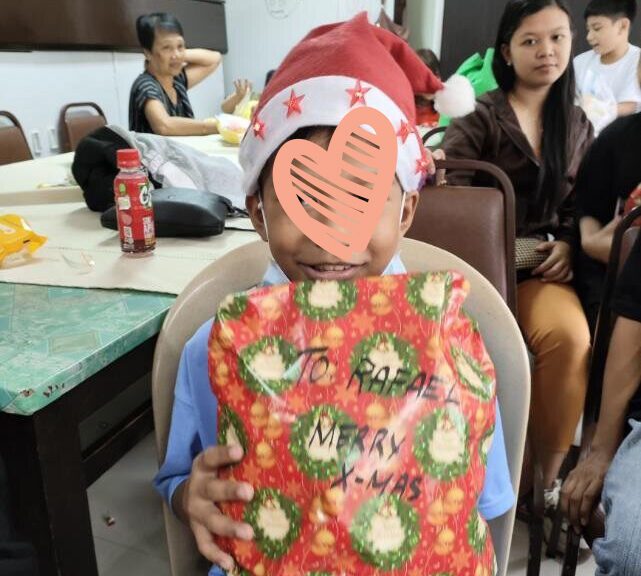 Little boy in Santa Hat holds up wrapped Christmas present