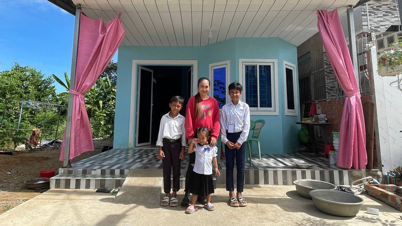 Family group stands in front of blue house with pink curtains