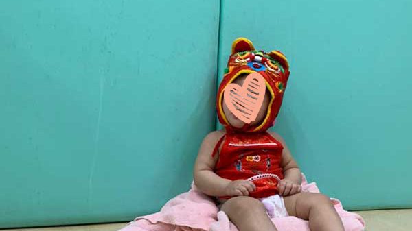 Little girl sits on a pink blanket in front of a blue wall.