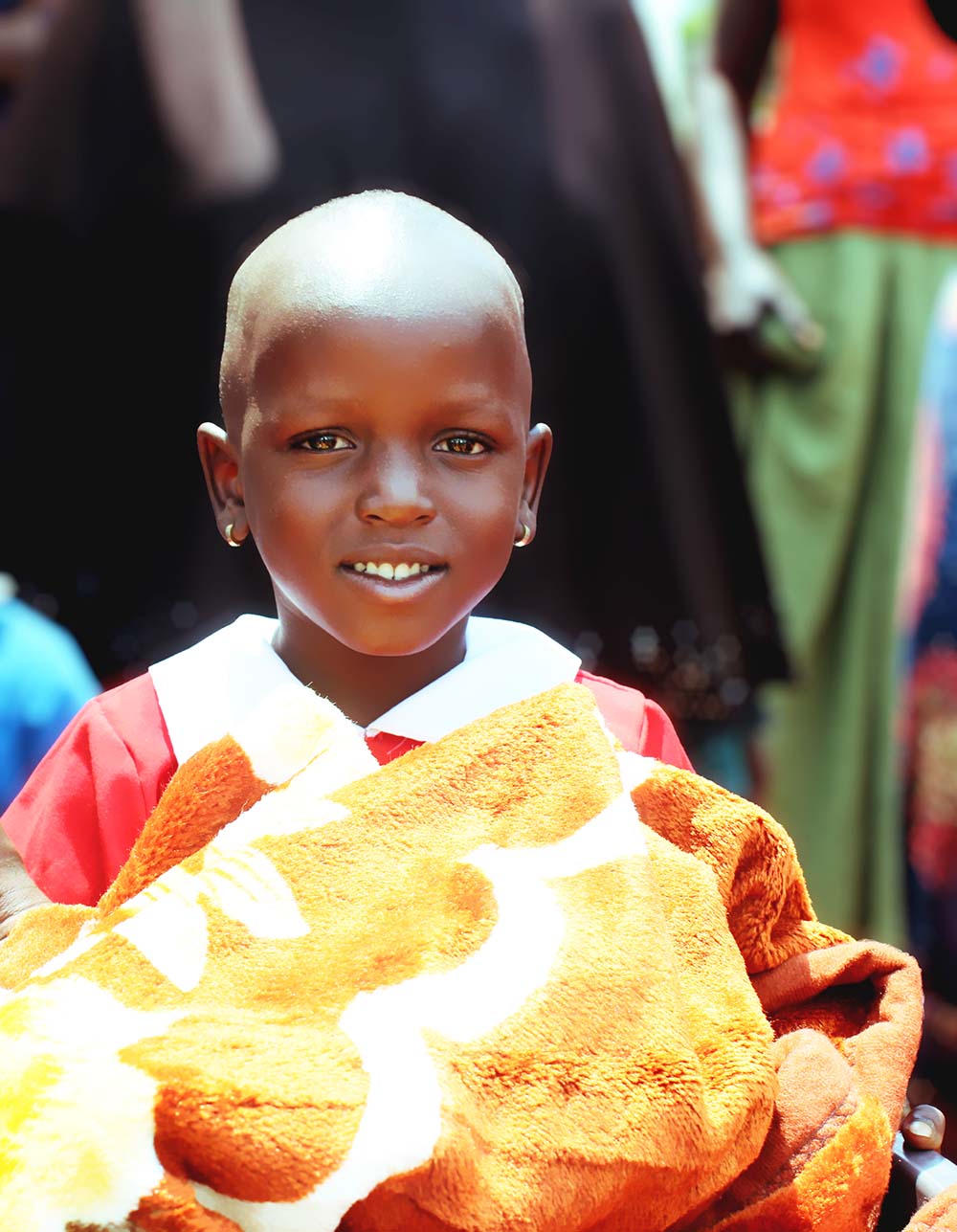 Little girl in red dress holds yellow blanket close and smiles