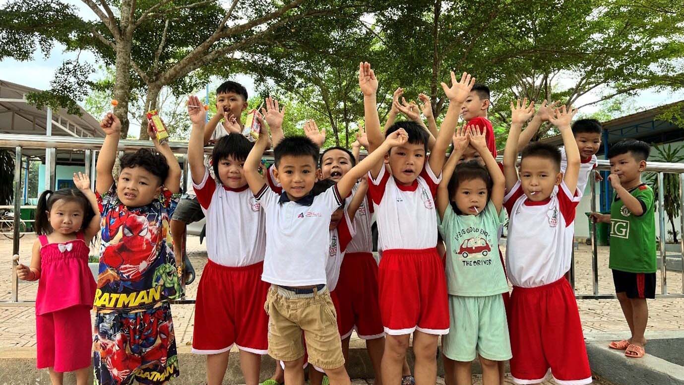 Group of children on a playground holds up hands and smile!