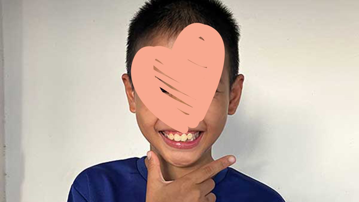 Little boy in blue shirt smiles and gestures with his hand