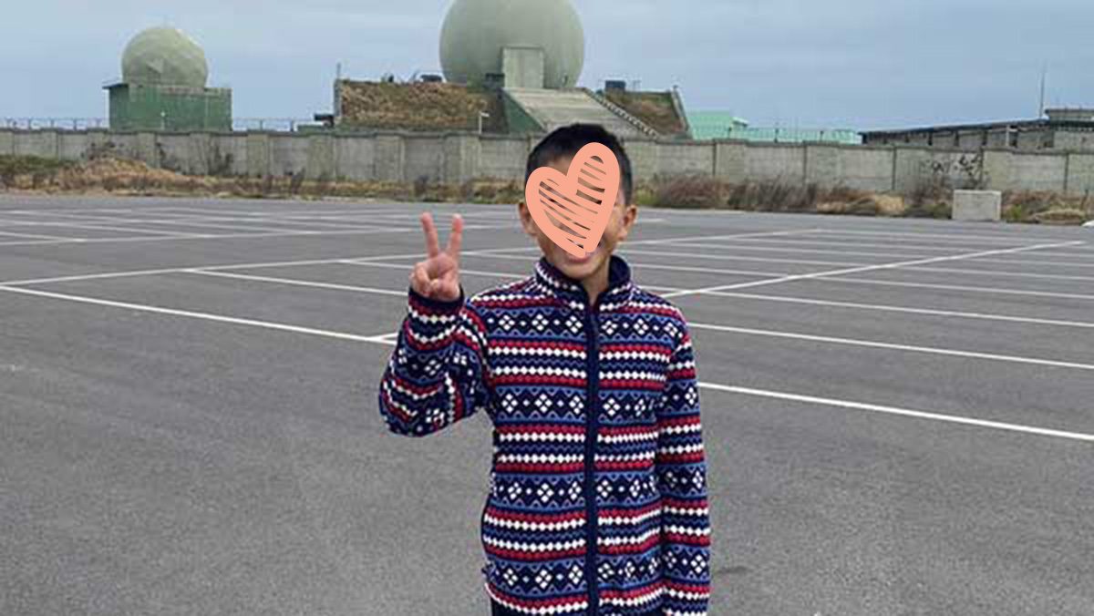 Young boy stands outside on pavement and holds up peace sign