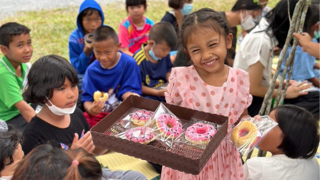 Cute little girl in a pink dress holding a tray of donuts