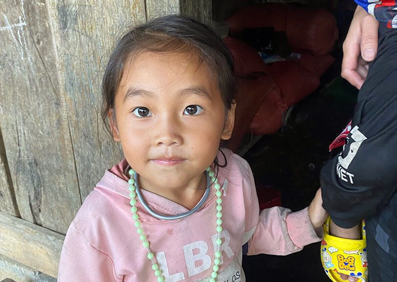 A little girl looks up at the camera in front of her house