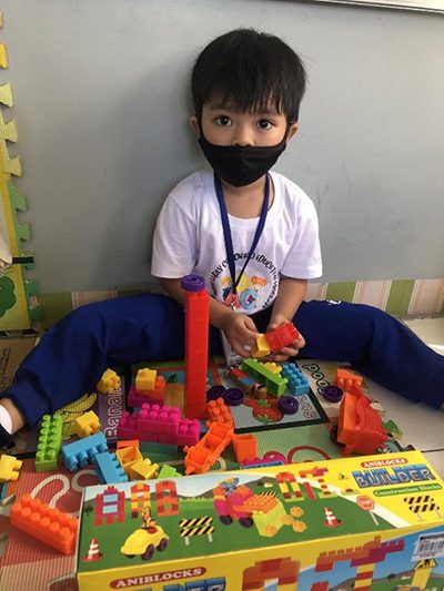 A little boy in a mask plays with Legos
