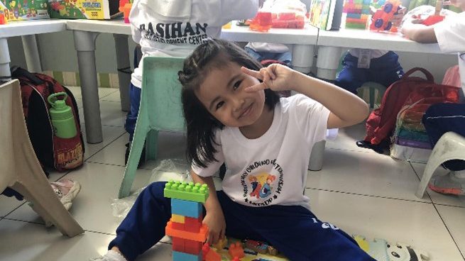 A little girl holds up a peace sign with legos in front of her