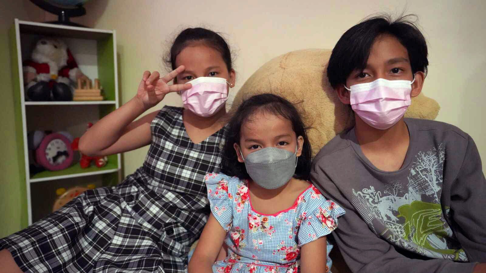 Two sisters and a brother wear face masks and pose for the camera