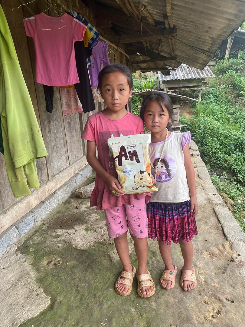 sisters stand outside of their home holding a bag of chips