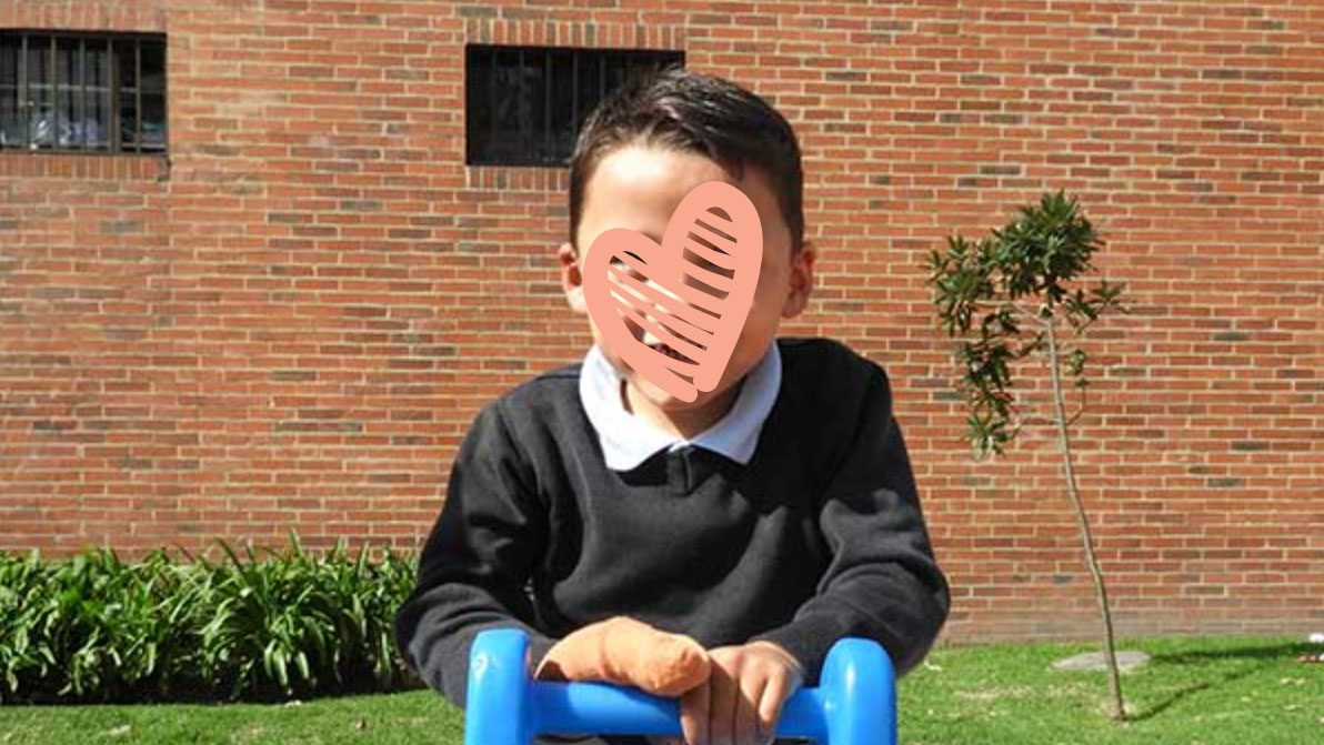 Little boy sits on a blue toy outside in front of a brick wall