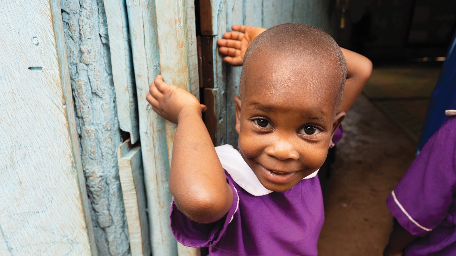 2023 annual report cover of a little girl in uganda in a purple dress leaning against a blue wall