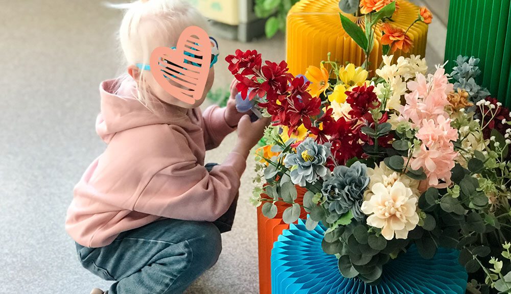 a child with a heart over her face crouches next to a flowerpot in china